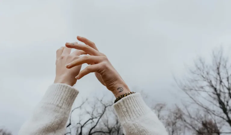 Petit tatouage lune à l’intérieur du poignet sur une femme portant un pull clair
