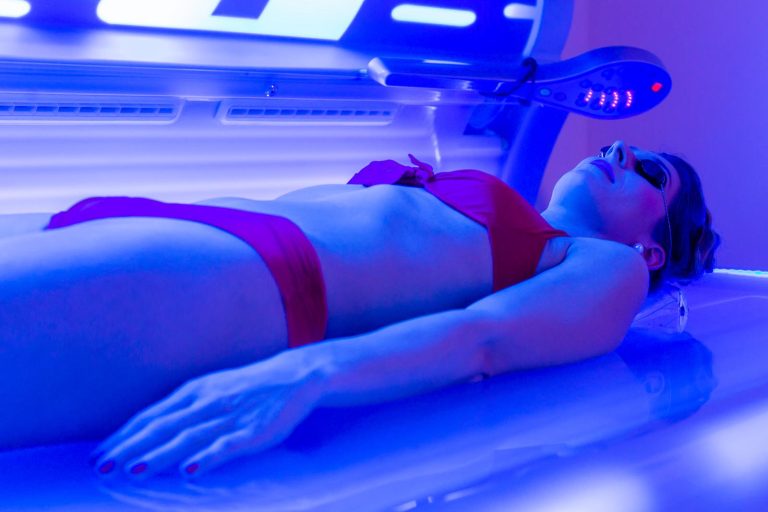 Femme en maillot avec lunettes de protection allongée dans une cabine UV pour une séance de bronzage"